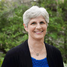 headshot of a woman with glasses and a green backdrop.